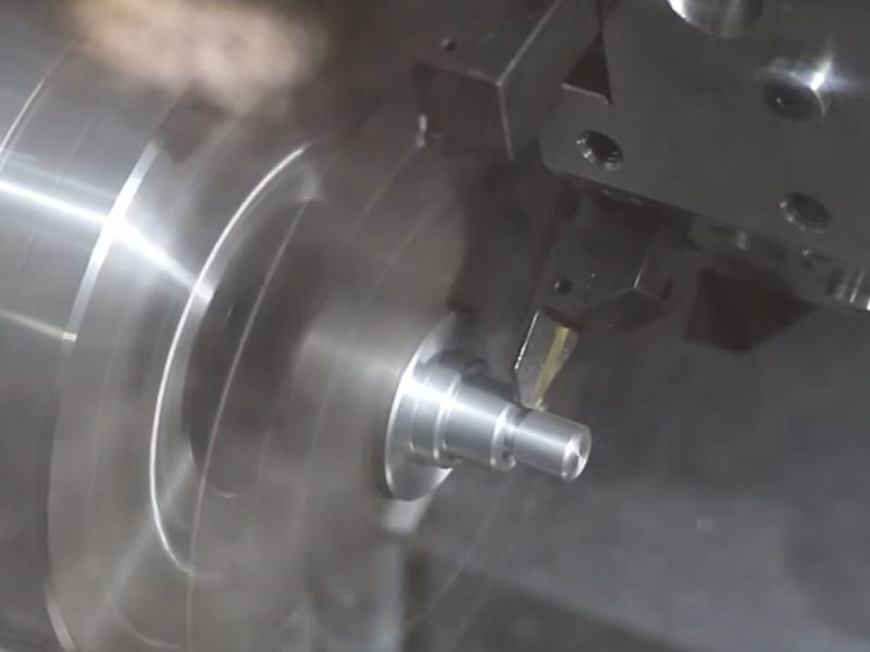 A turning insert cutting a stepped shaft on a CNC lathe, the workpiece
                      spinning in the chuck with the finished diameters visible behind the
                      tool.