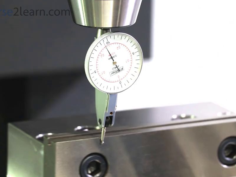 A dial test indicator held in the spindle of a milling
                        machine, its contact point resting against the fixed jaw
                        of a vise, with the dial reading close to zero.