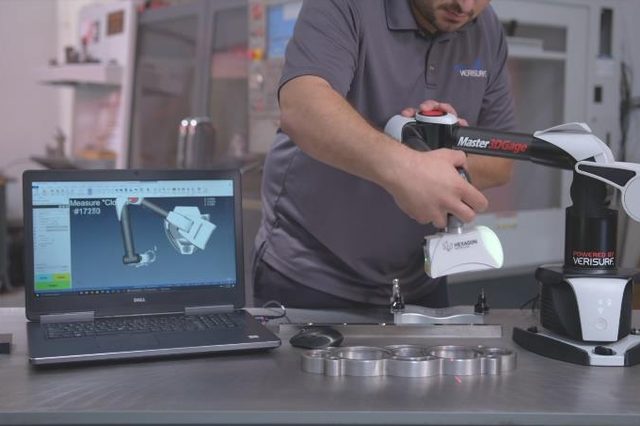 A technician measures a machined aluminium part with a Master3DGage
                      portable measuring arm. The laptop beside them shows the Verisurf
                      screen with the part model and the feature being measured.